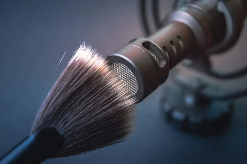 close-up of a makeup brush gently touching a professional microphone in a dimly lit ASMR recording setup