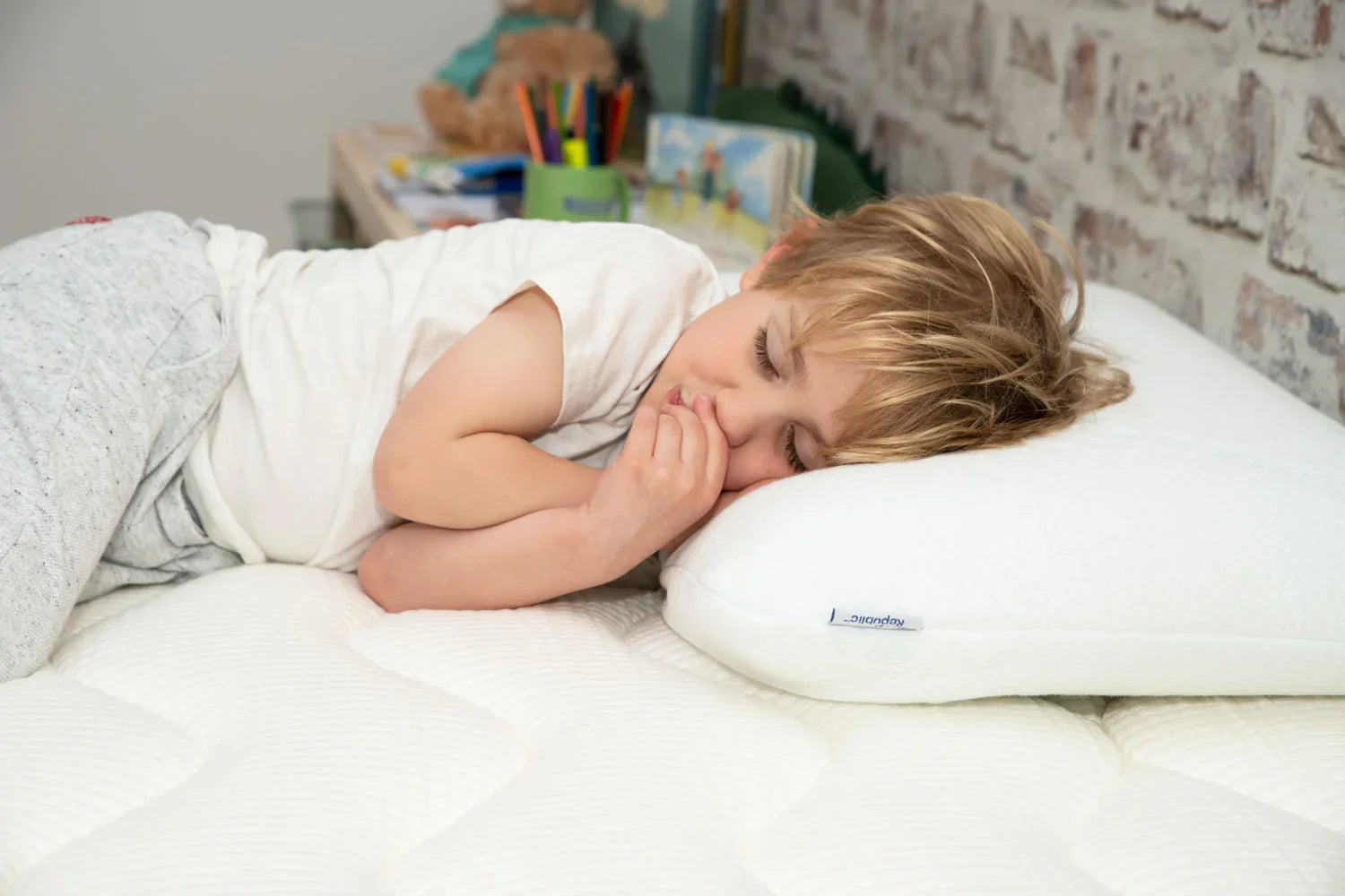 Child sleeping on a white orthopedic pillow and mattress in a cozy bedroom with brick wall