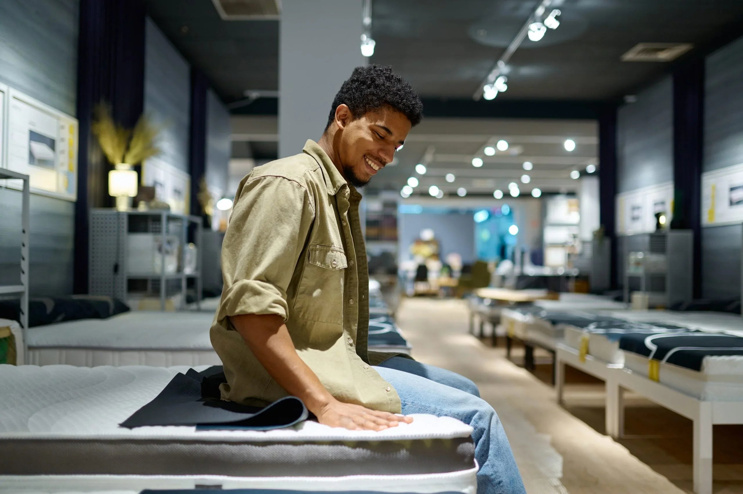 Smiling man testing mattress comfort in a well-lit mattress showroom