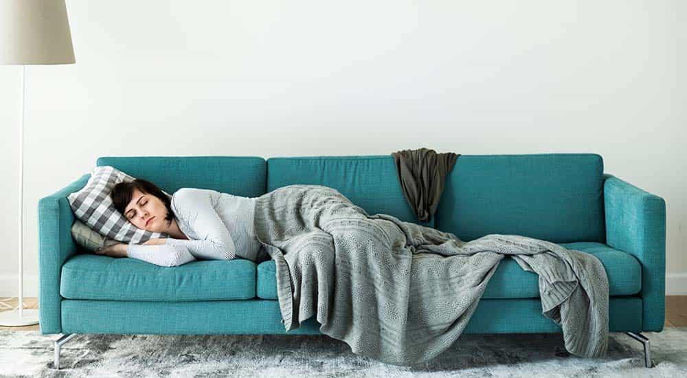 Woman sleeping on teal sofa with gray knitted blanket and checkered pillow in minimalist living room
