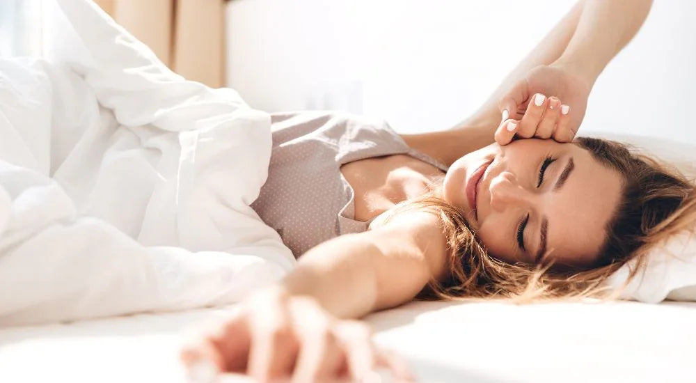 Woman stretching and waking up smiling in bright bedroom with white bedding