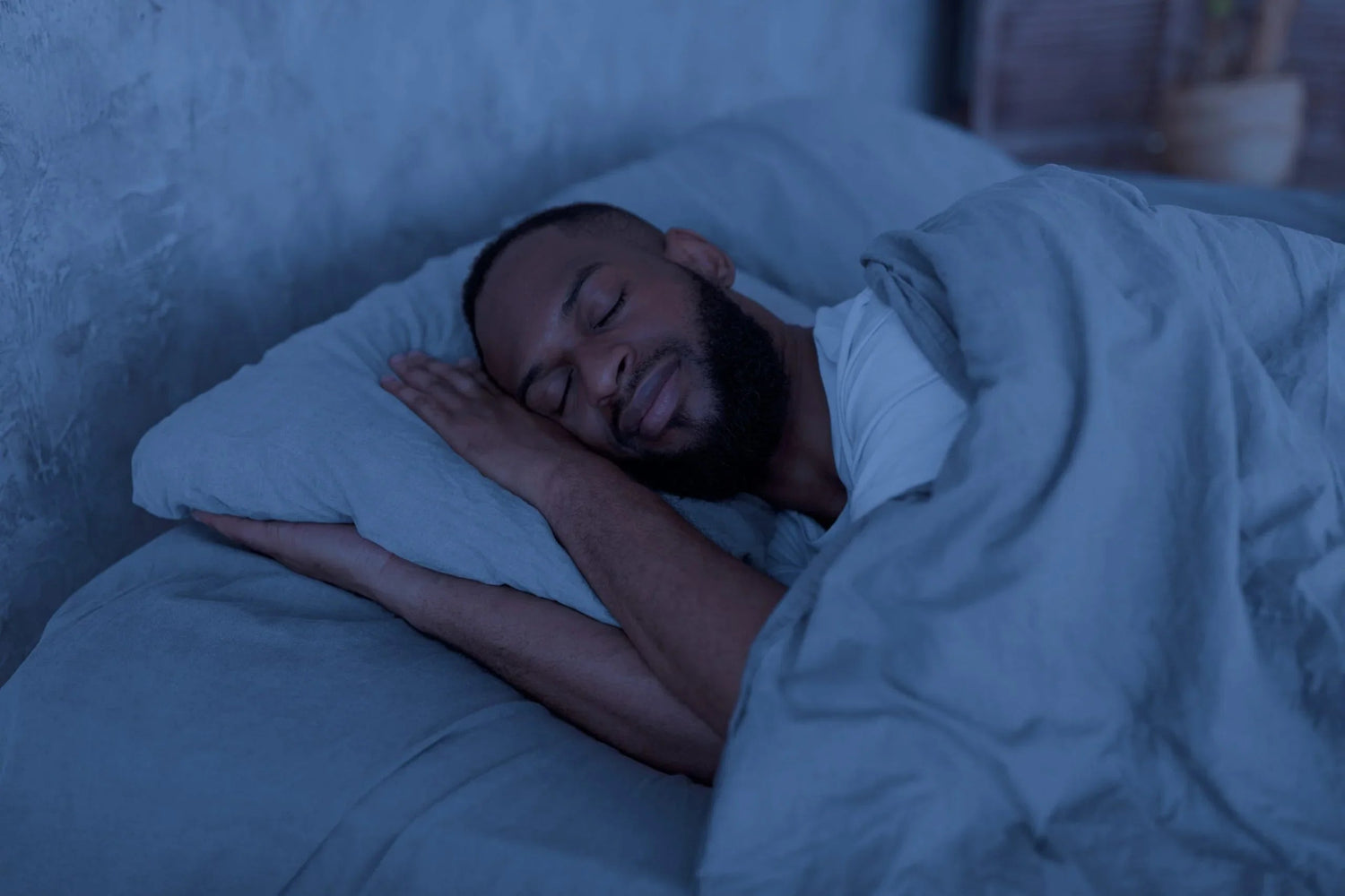 Man sleeping peacefully on his side in bed with gray sheets and blanket at night