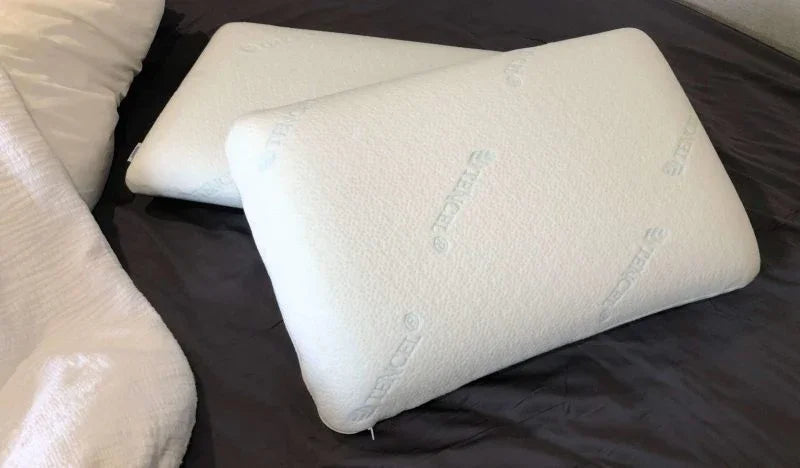 Two white memory foam pillows on a dark bedspread with textured pillow covers