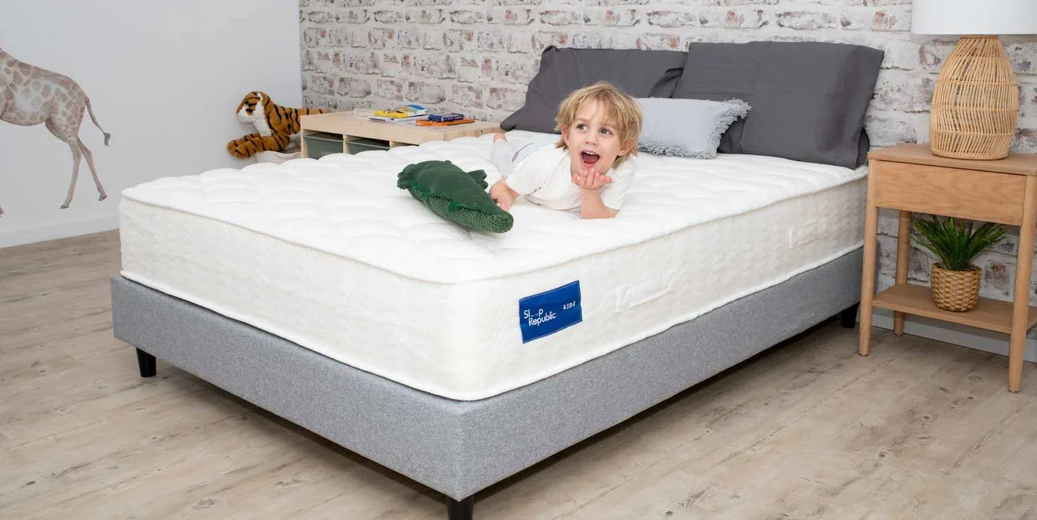 Child lying on white kids mattress with gray bed frame in bright modern bedroom