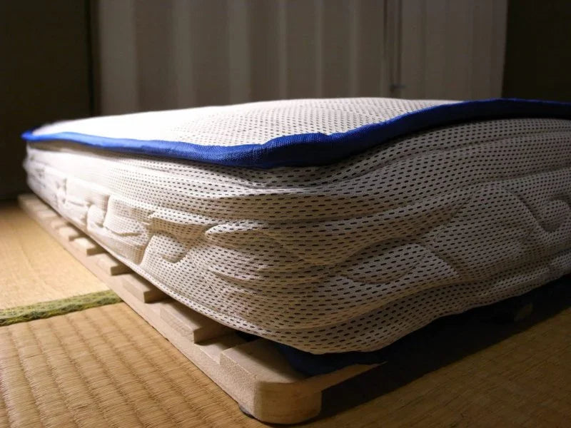 Close-up of a thick white mattress with blue trim on a wooden slatted bed frame in a tatami room