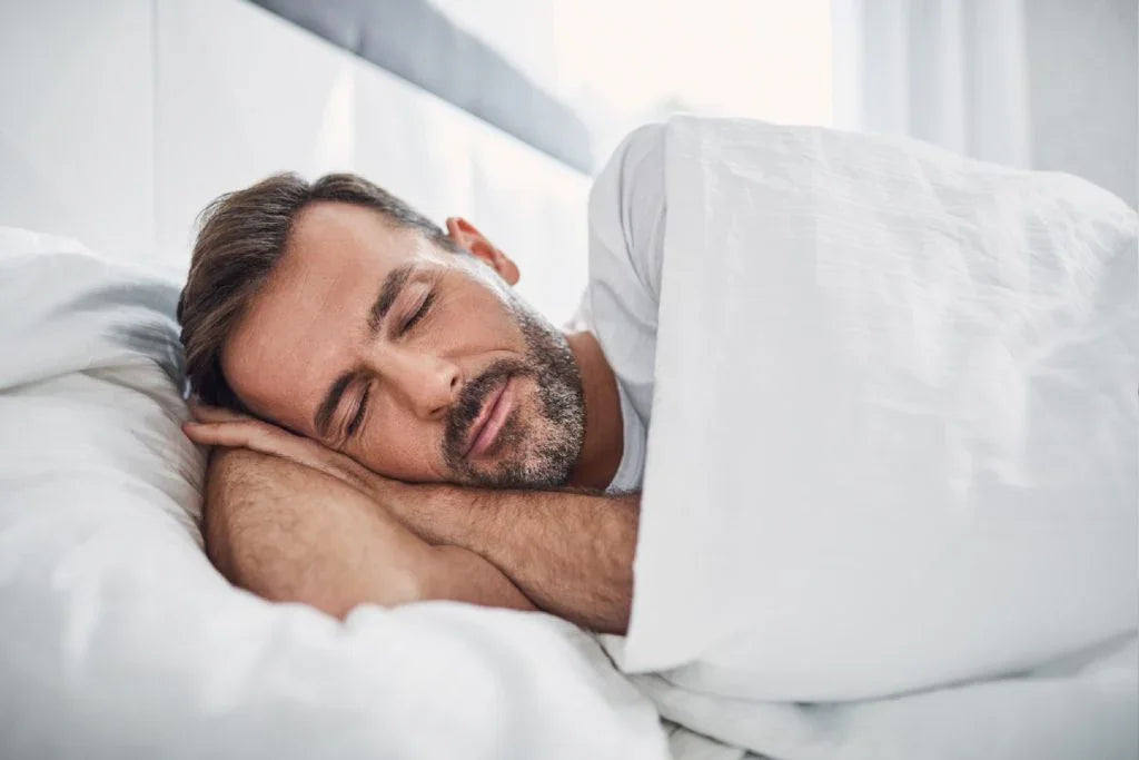Man with beard peacefully sleeping in white bed with white bedding and pillow