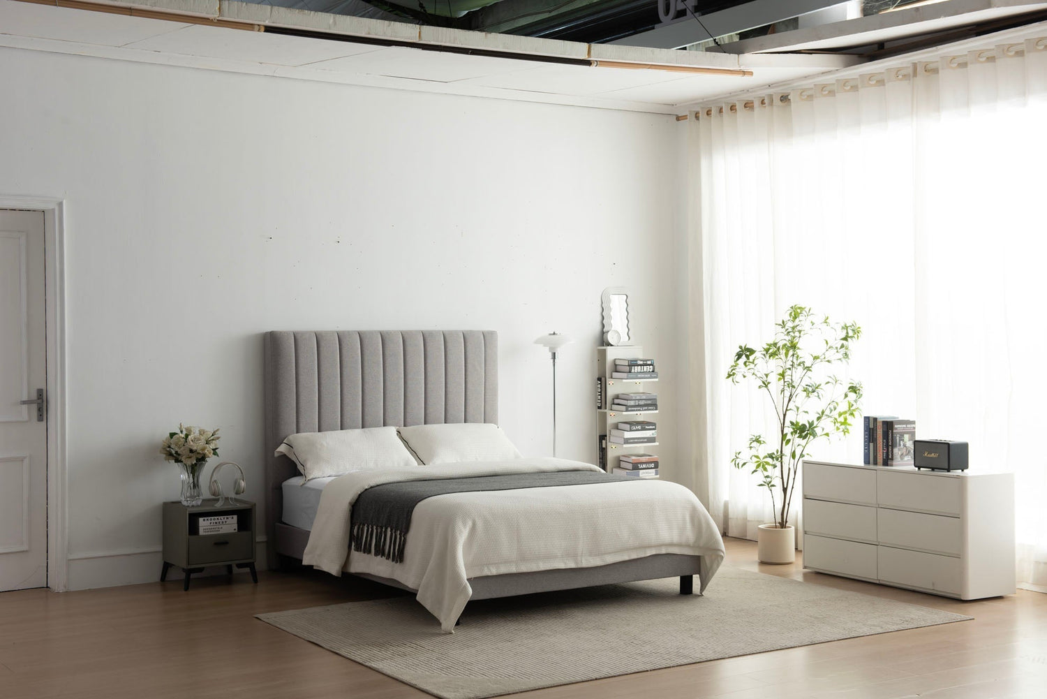 Modern minimalist bedroom with gray upholstered bed, white bedding, bedside table, and natural light