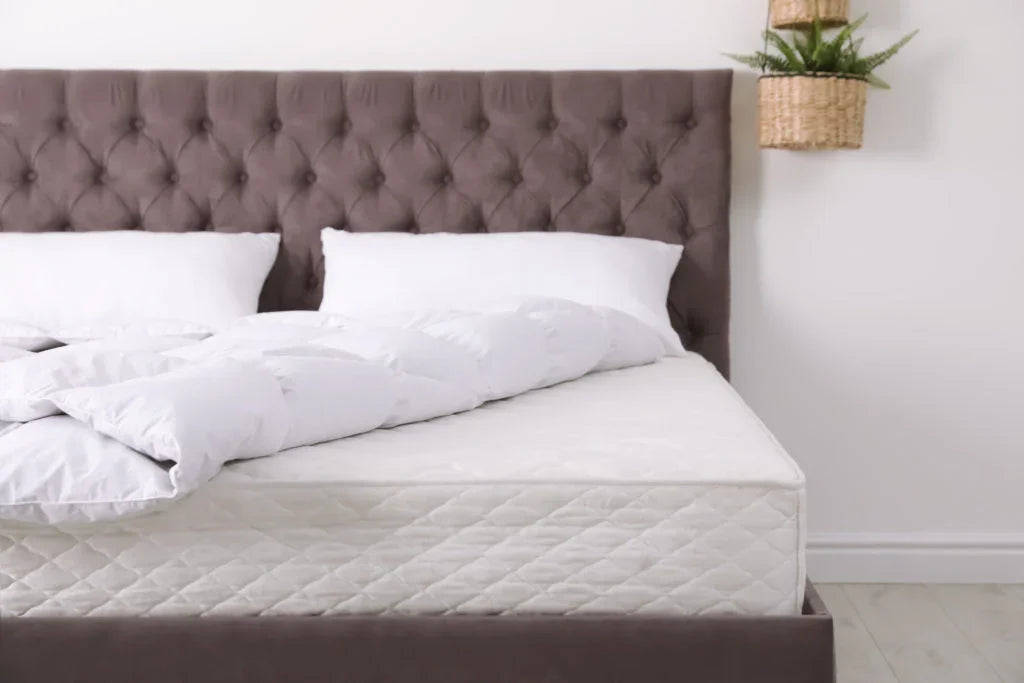 Modern bedroom with tufted brown headboard, white pillows, white comforter, and mattress