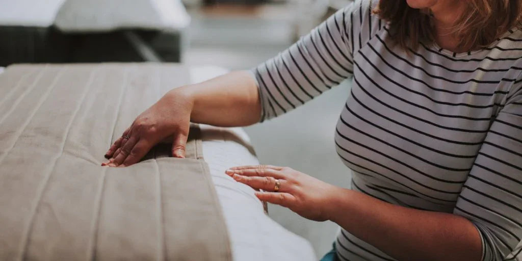 Woman in striped shirt touching mattress surface in a bedroom setting