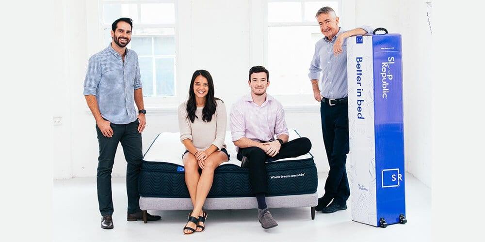Group of four people around a Sleep Republic mattress and boxed bed in a bright white room