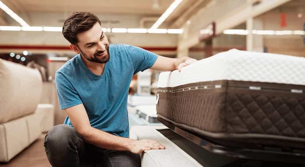 Man testing a hybrid memory foam mattress in a well-lit furniture store showroom