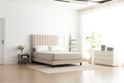 Beige upholstered bed in a modern bedroom setting with white walls and minimal decor.