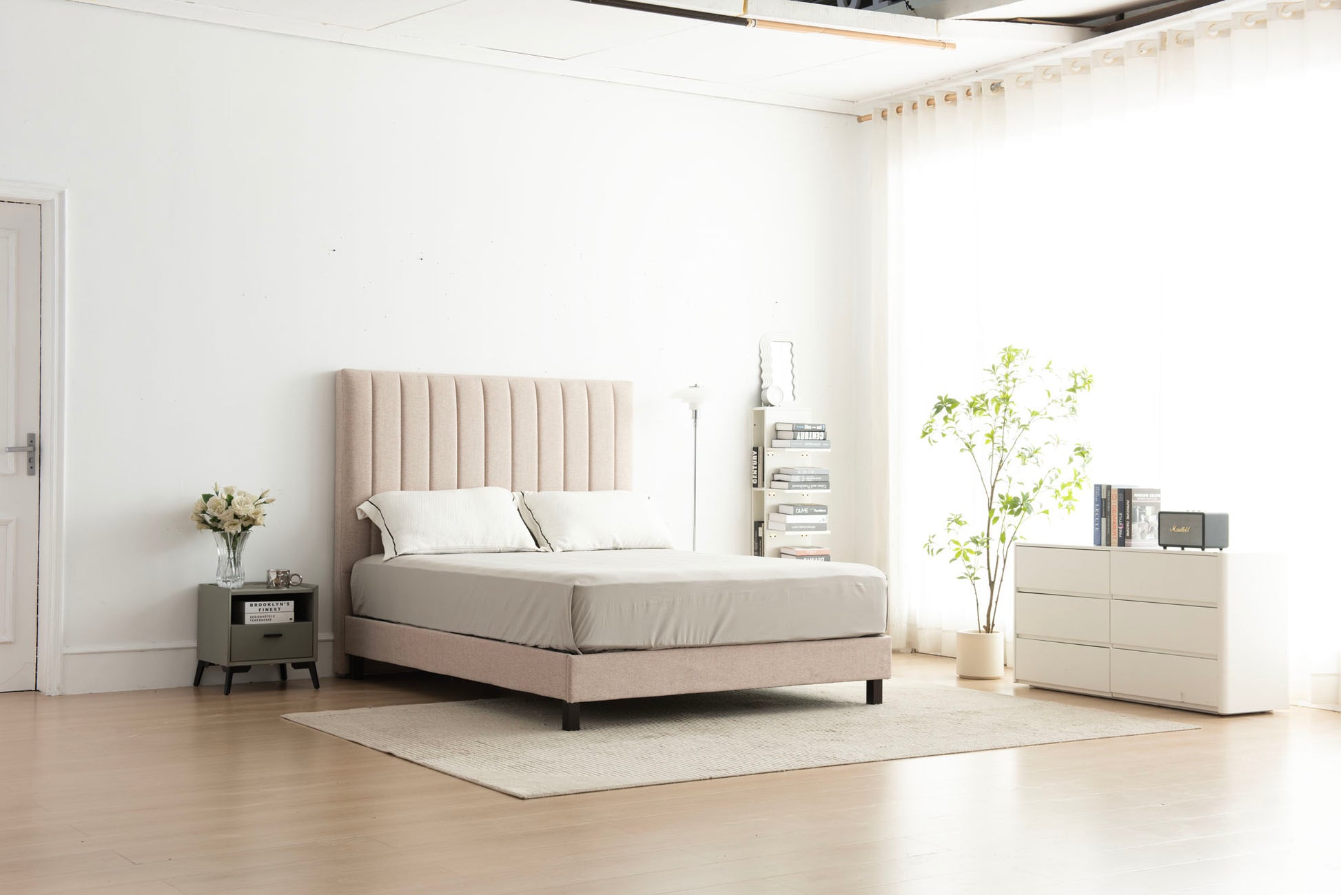 Beige upholstered bed in a modern bedroom setting with white walls and minimal decor.