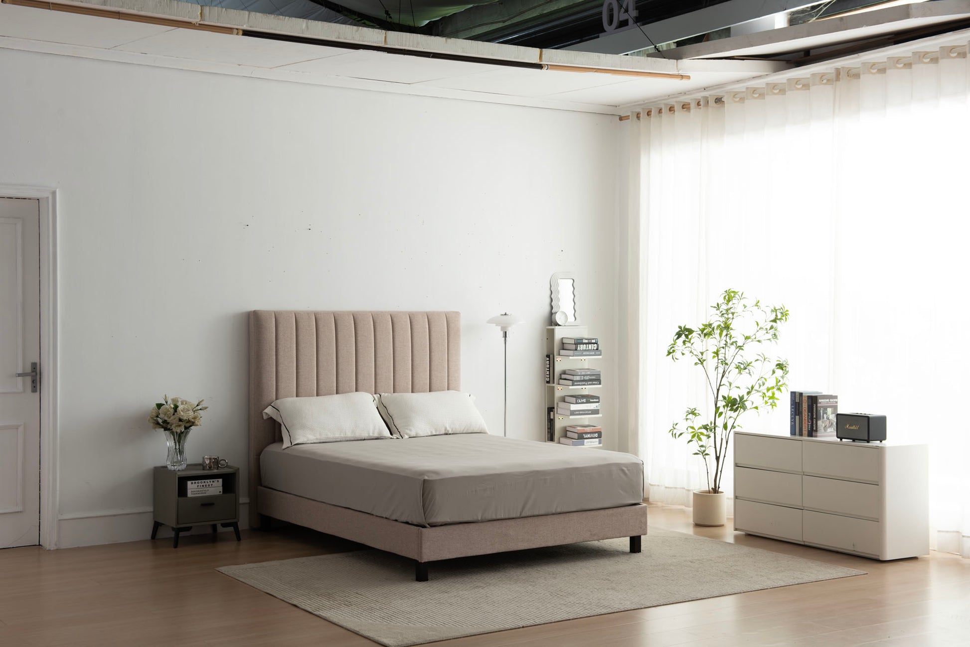 Modern bedroom with a beige upholstered bed, white dresser, and decorative items.